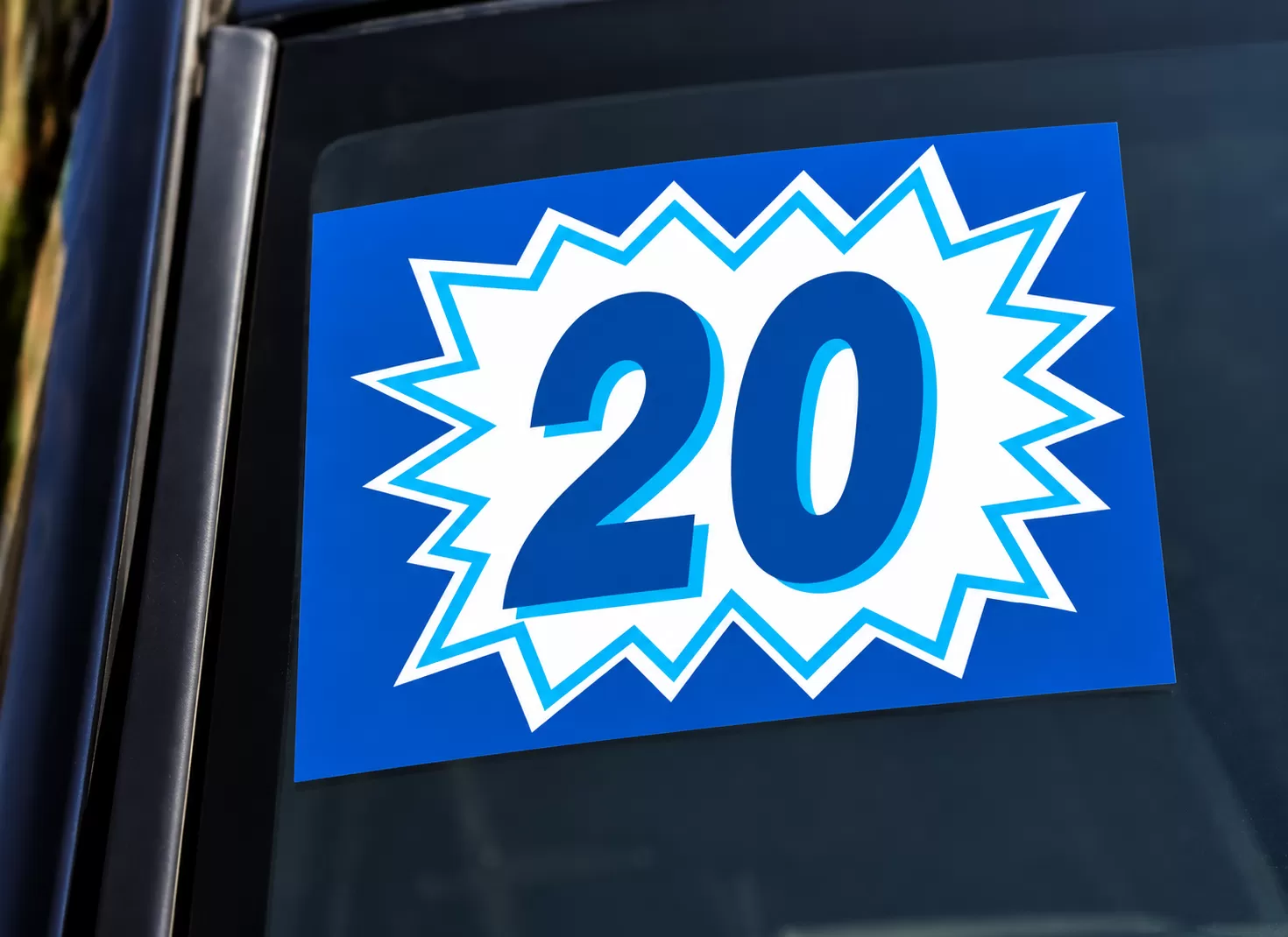 Blue and white burst model-year sticker showing 20 on a vehicle windshield
