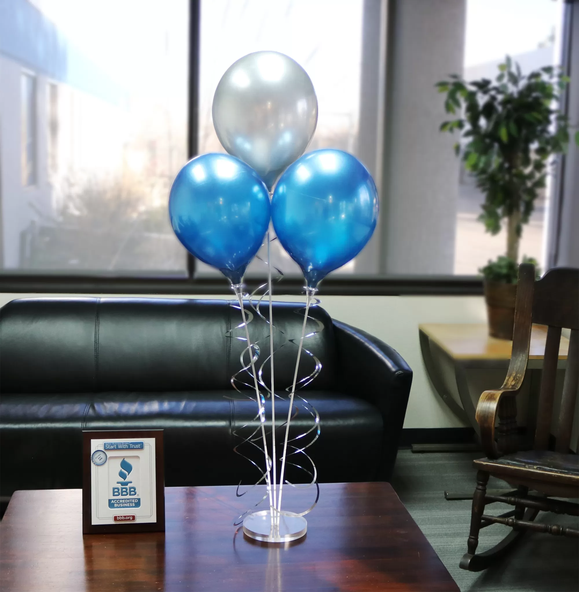 Two blue and one silver PermaShine balloons on a clear acrylic weighted base