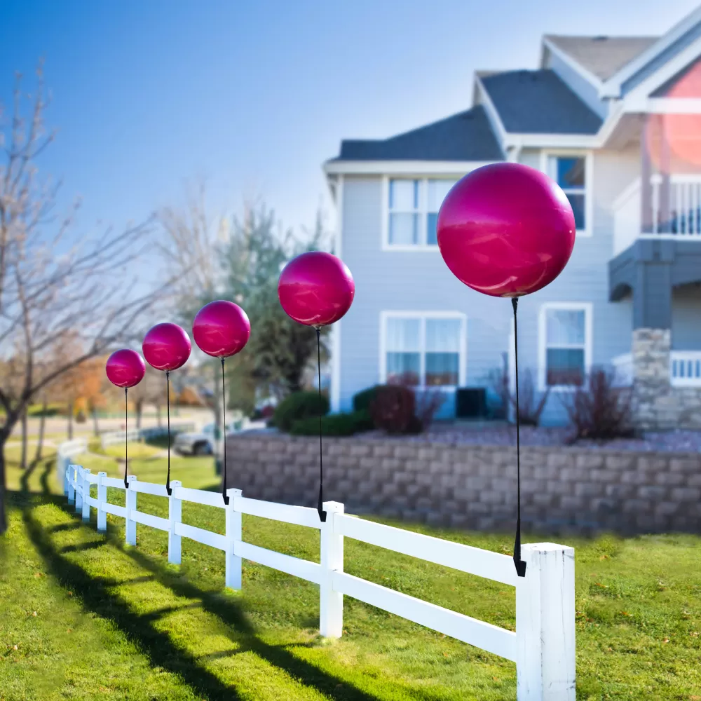Pink DuraBalloons on vertical brackets along a white fence